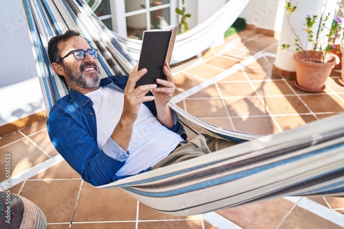 Fotografia Middle age man reading book lying on hammock at terrace home
