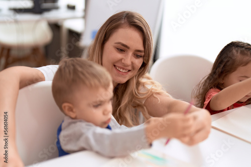 Teacher with boy and girl sitting on table drawing on paper at kindergarten