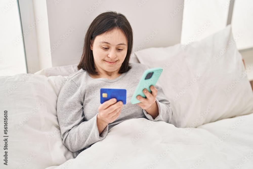 Young woman with down syndrome using smartphone and credit card sitting on bed at bedroom Young woman with down syndrome using smartphone and credit card sitting on bed at bedroom