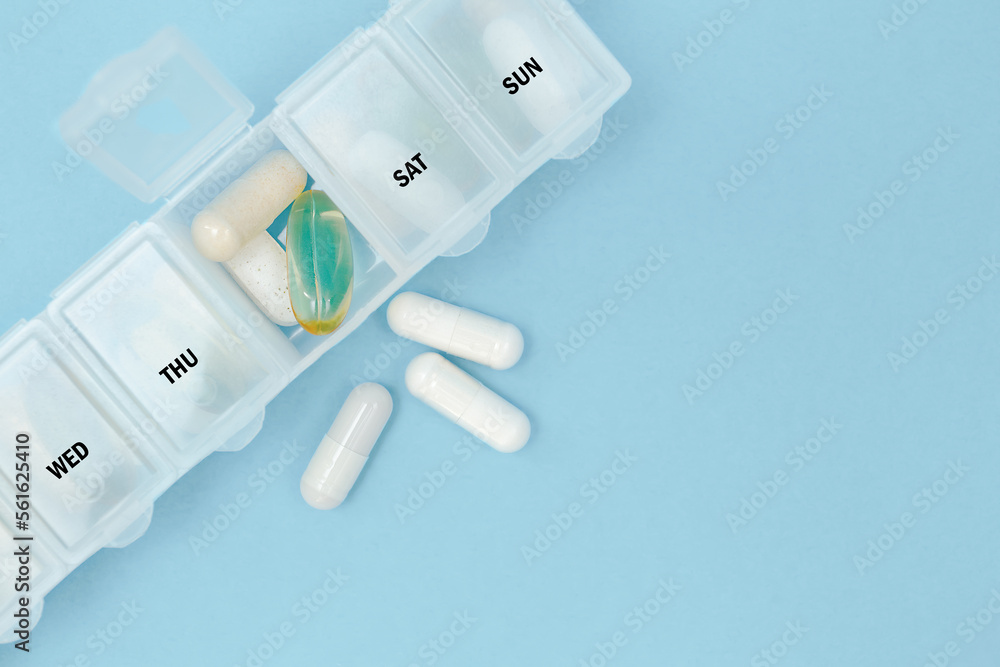 Pill organizer with variety of pills and supplement. Weekly pill organizer or daily pill box with medications on blue background. Copy space, space for text, top view. Pill organizer with variety of pills and supplement. Weekly pill organizer or daily pill box with medications on blue background. Copy space, space for text, top view.