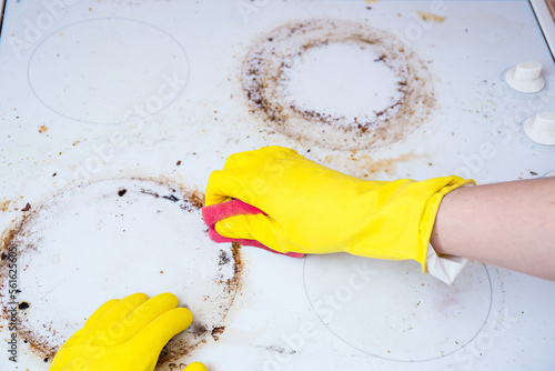 Man cleaning ceramic modern stove or hob with detergent agent. Hand in yellow gloves clean stove from burnt and grease dirt. Housework, professional cleaning service after tenants.