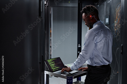 Side view portrait of black man as network engineer using laptop while setting up servers in data center