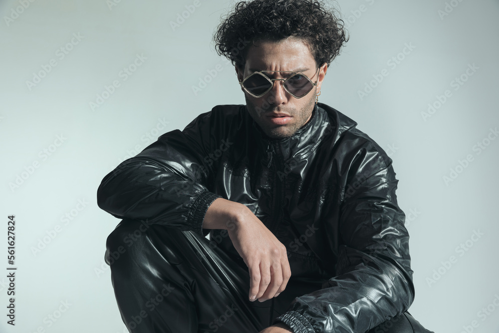 Obraz premium confident man with sunglasses wearing leather outfit and posing with elbow on knee
