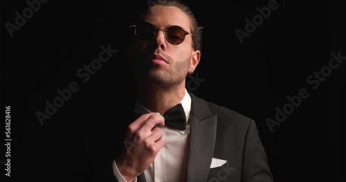 project video of elegant man arranging tuxedo and bowtie, wearing sunglasses and posing in a cool way in front of black background photo