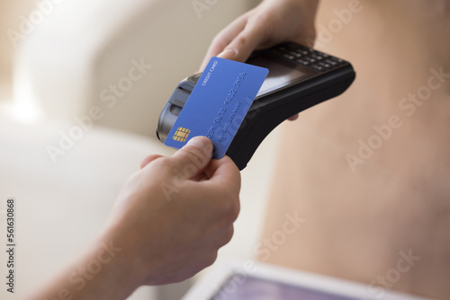Fotografia Hand of bank cardholder paying bill in cafe, applying blue credit card with chip at wireless payment terminal held by waitress, using electronic transaction banking technology