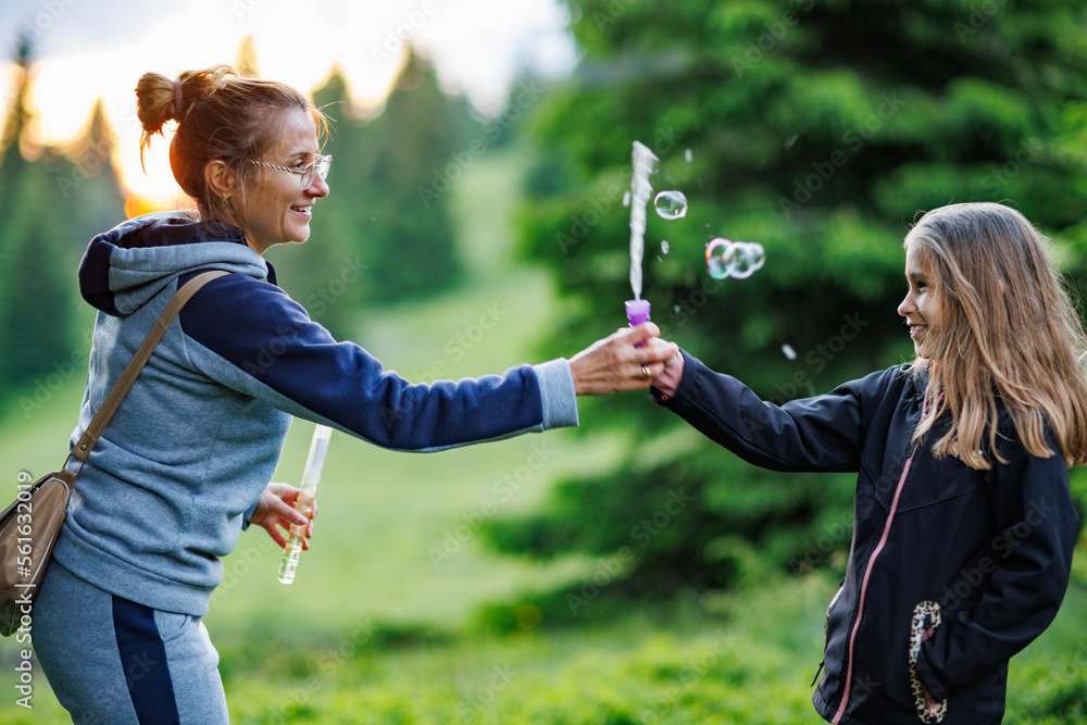 Foto de Mother and her daughter blow soap bubbles in the spruce forest during a walk do Stock