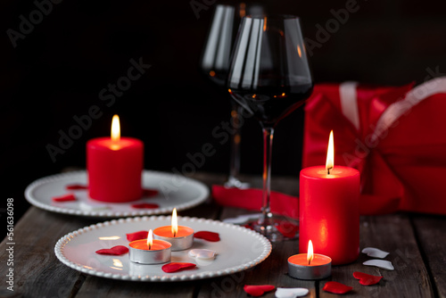Saint Valentine's Day celebration. Red burning candles, hearts, gift box, postcard on dark wooden background. Happy holiday . Table decor for festive dinner, romantic atmosphere