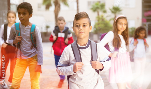 Portrait of positive boy standing near school, children on background