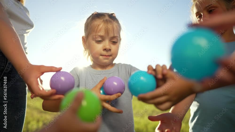 Happy children play together and have fun in the park with colorful balls. Girl collects small balls from children. Teamwork of children in park on the grass. Happy child playing with colored balloons Happy children play together and have fun in the park with colorful balls. Girl collects small balls from children. Teamwork of children in park on the grass. Happy child playing with colored balloons