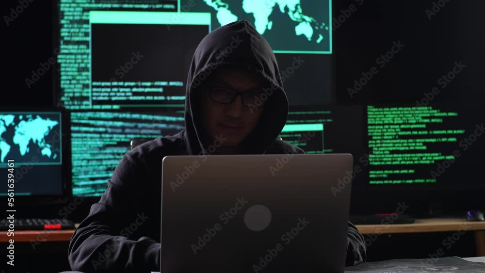 Asian Male Hacker In A Hood Looking At Camera While Works On A Laptop With Maps And Data On Display Screens Of Multiple Monitors In A Dark Office Room
Asian Male Hacker In A Hood Looking At Camera While Works On A Laptop With Maps And Data On Display Screens Of Multiple Monitors In A Dark Office Room