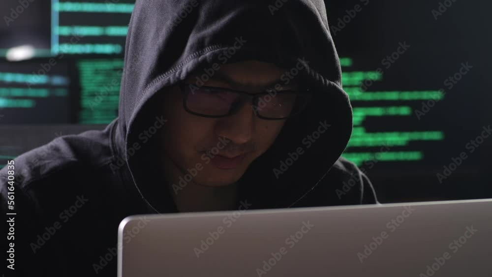 Close Up Of Asian Male Hacker In A Hood Looking At Camera And Crossing His Arms While Works On A Laptop With Maps And Data On Display Screens Of Multiple Monitors In A Dark Office Room
Close Up Of Asian Male Hacker In A Hood Looking At Camera And Crossing His Arms While Works On A Laptop With Maps And Data On Display Screens Of Multiple Monitors In A Dark Office Room