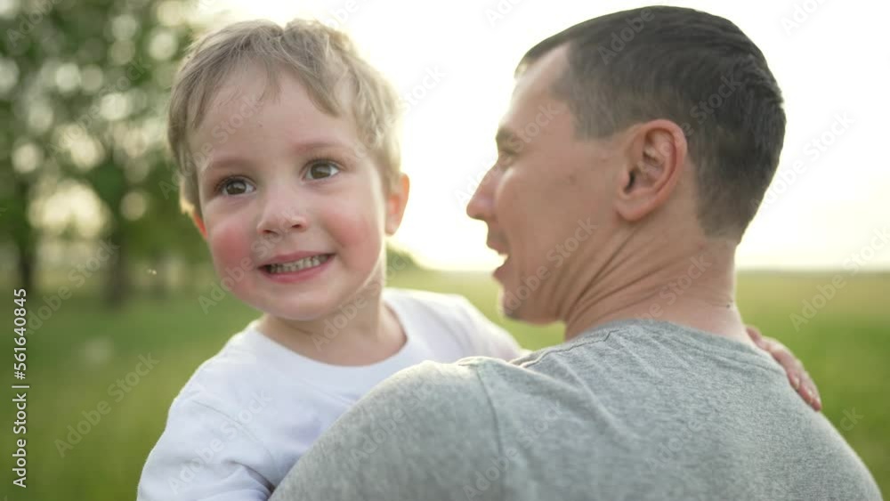 Happy family concept. family support for children. Dad and son play in the park in summer. Father's Day. Father and son family picnic. Sunset walk on green grass. Dad holding the boy's son in his arms Happy family concept. family support for children. Dad and son play in the park in summer. Father's Day. Father and son family picnic. Sunset walk on green grass. Dad holding the boy's son in his arms