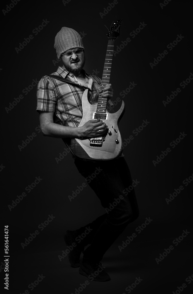 Fashionable bearded guy plays rock guitar on dark gray background, black and white monochrome photo