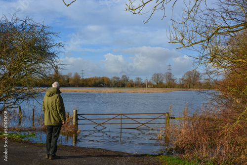 A man is looking at a flooded field after heavy rainfall. Rural Oxfordshire in winter..	