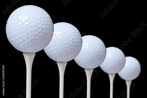 A closeup of five golf balls on a tees. black background.