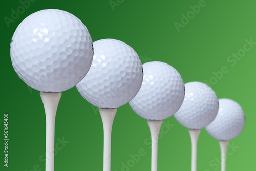 A closeup of five golf balls on a tees. green background.
