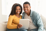 Cheerful young african american family look at tablet, make video call, surfing in internet, chatting online