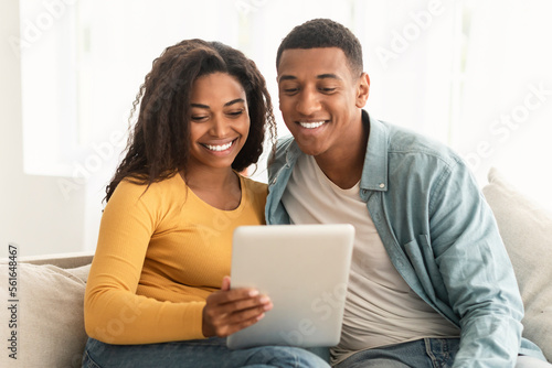 Cheerful young african american family look at tablet, make video call, surfing in internet, chatting online