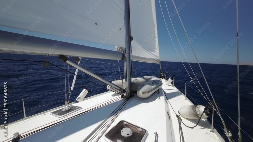 Floating sailing yacht with spread sails splitting the sea waves and an island on the horizon. Sail yacht floats by the storming sea. Bow of the boat cutting through the sea. Summer vacation shots. Floating sailing yacht with spread sails splitting the sea waves and an island on the horizon. Sail yacht floats by the storming sea. Bow of the boat cutting through the sea. Summer vacation shots.