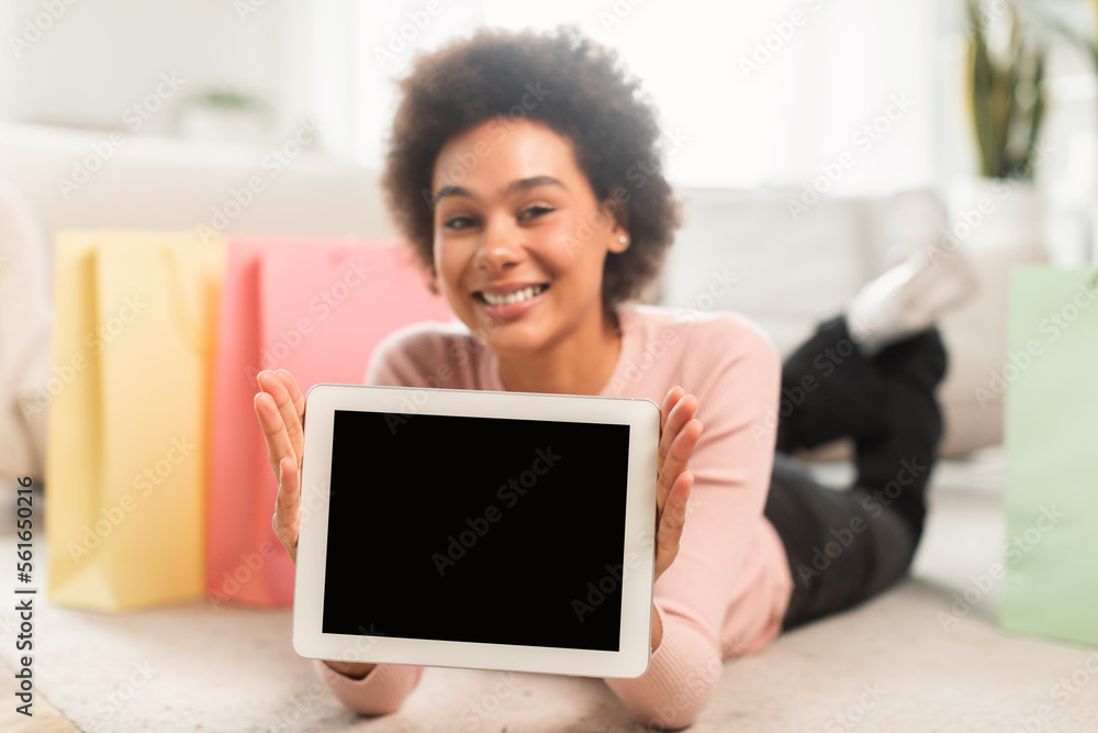 Smiling young mixed race female shopaholic fashion blogger show tablet with empty screen, lies on floor Smiling young mixed race female shopaholic fashion blogger show tablet with empty screen, lies on floor