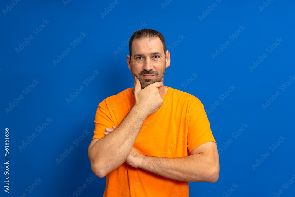 Curious handsome bearded latino man thinking with hand touching chin on isolated studio blue background. Curious handsome bearded latino man thinking with hand touching chin on isolated studio blue background.
