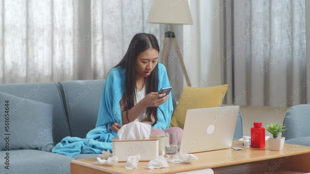 Sick Asian Woman With Blanket Using Smartphone While Sitting On Sofa Works On A Laptop Computer In The Living Room At Home
Sick Asian Woman With Blanket Using Smartphone While Sitting On Sofa Works On A Laptop Computer In The Living Room At Home