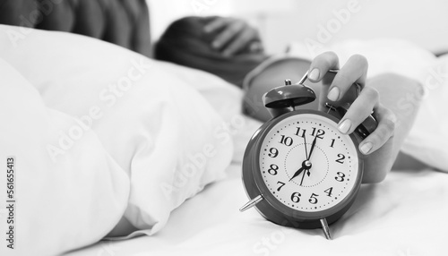 Woman turning off alarm clock in bedroom, selective focus. Black and white photography