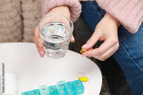 Woman taking pill from plastic container at white table indoors, closeup