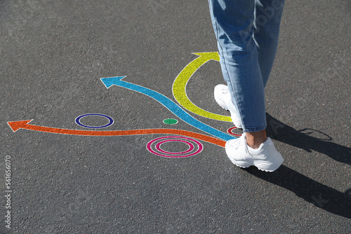 Choice of way. Woman walking towards drawn marks on road, closeup. Colorful arrows pointing in different directions photo