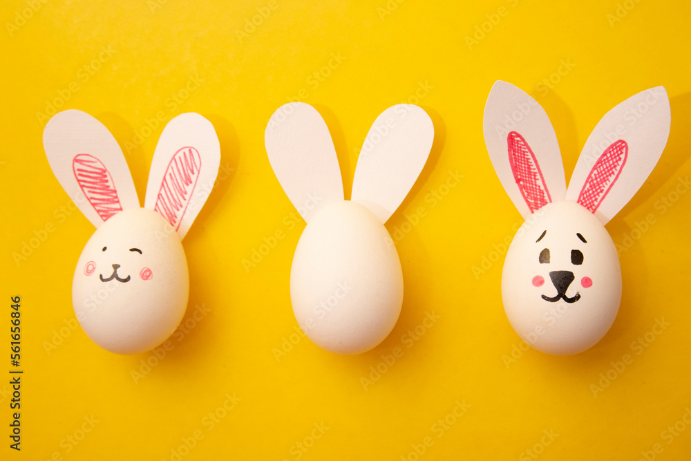 Food photo for Happy Easter. Chicken egg with cute rabbit faces and bunny ears on yellow background. White empty egg for coloring for children. Banner. Greeting card for celebration. Copyspace. Gift Food photo for Happy Easter. Chicken egg with cute rabbit faces and bunny ears on yellow background. White empty egg for coloring for children. Banner. Greeting card for celebration. Copyspace. Gift