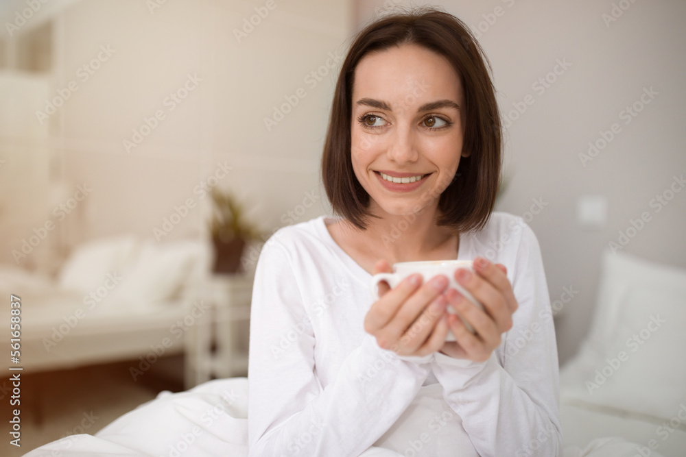 Headshot of cheerful young woman drinking herbal tea in bed Headshot of cheerful young woman drinking herbal tea in bed