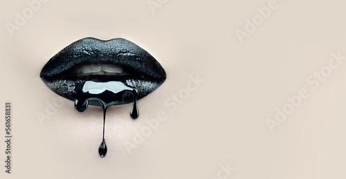 Black Paint dripping from the lips, dark liquid drops on beautiful model girl's mouth on beige background. Halloween party make-up, gothic style. Beauty makeup close up. Wide screen art backdrop. 