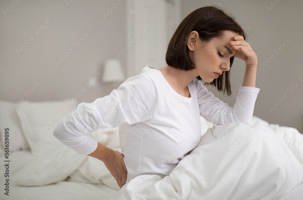 Unhappy woman suffering from back pain at home in bedroom Unhappy woman suffering from back pain at home in bedroom