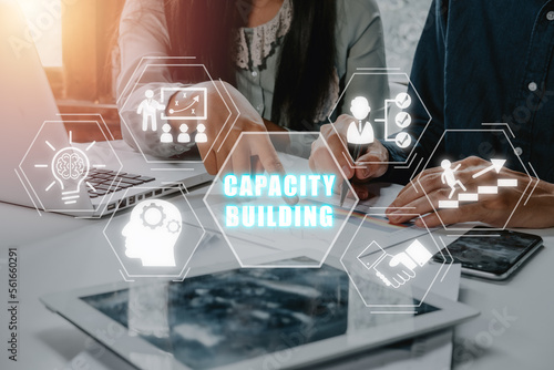 Capacity building concept, Mature businessman discuss information with a younger colleague with virtual graphic capacity building icon diagram.