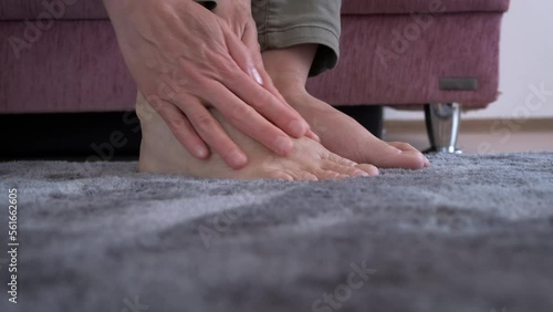 Lady suffering from feet ache. A woman suffering from feet ache try to reduce the pain with massage in the room. photo