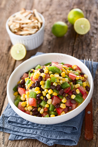 Mexican style colorful fresh vegetable salad made of beans, corn, tomato and bell pepper served in bowl, fork on the side, photographed on wood (Selective Focus, Focus on the front of the salad)