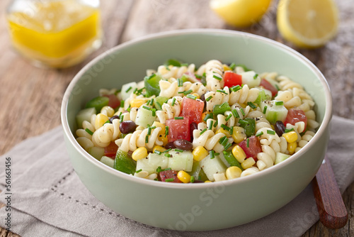 Fresh homemade colorful vegan fusilli pasta salad with beans, corn, tomato, cucumber and green bell pepper, photographed on wood (Selective Focusone third into the salad)