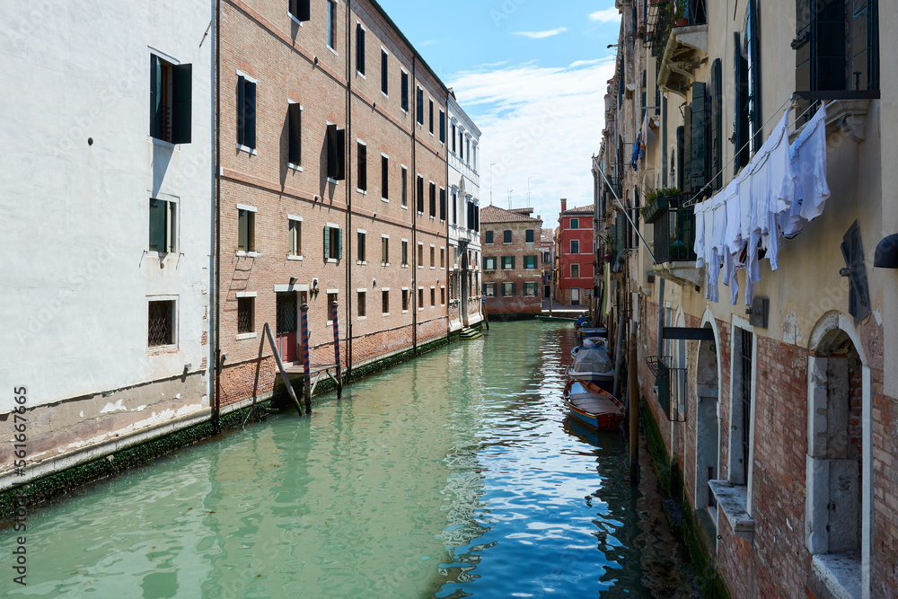 Obraz premium Beautiful, tranquil view in Venice, Italy, with boats parked on canal surrounded by picturesque old buildings under blue sky on spring day.