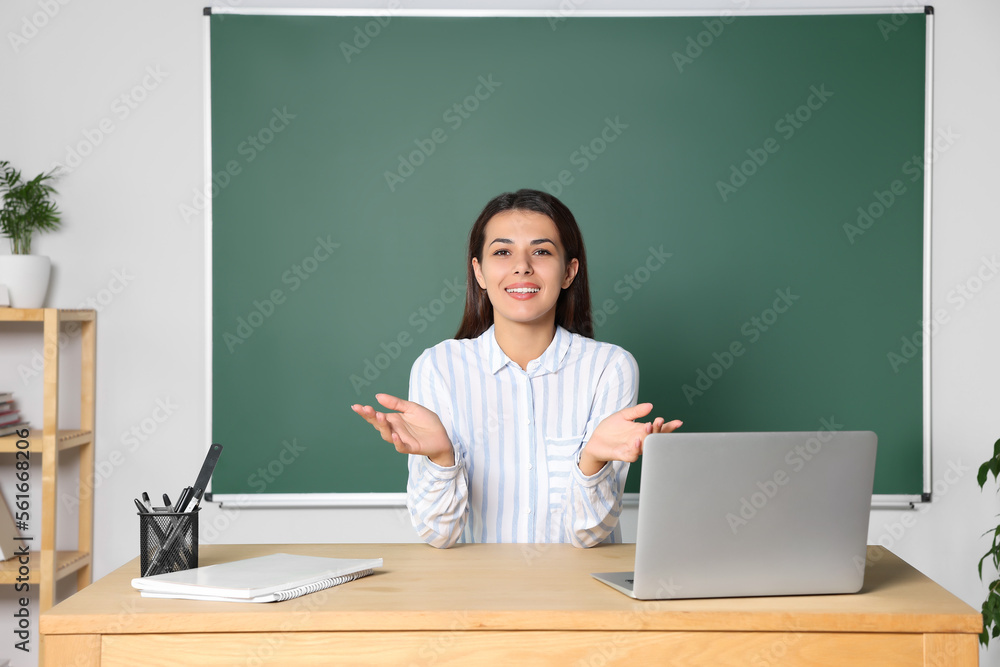 Happy young teacher explaining something at table in classroom Happy young teacher explaining something at table in classroom