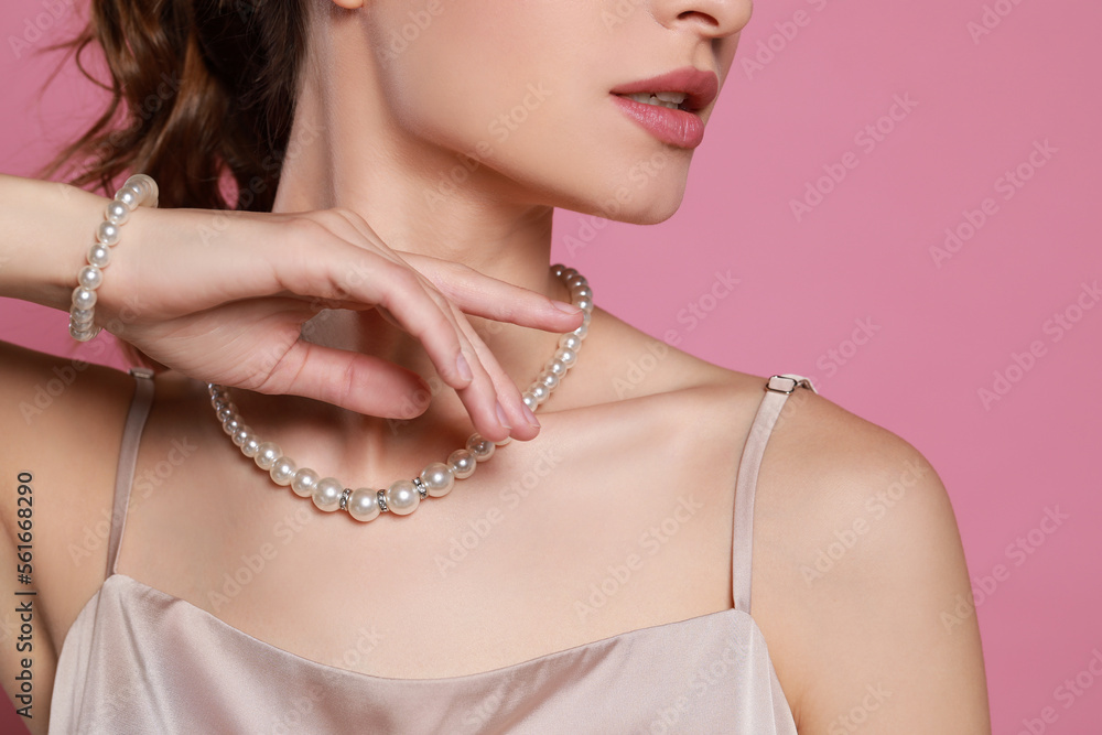 Young woman wearing elegant pearl jewelry on pink background, closeup