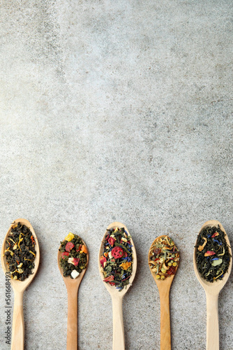 Different kinds of dry herbal tea in wooden spoons on light grey table, flat lay. Space for text