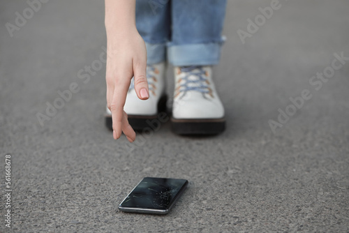 Woman taking dropped smartphone from asphalt, closeup. Device repairing