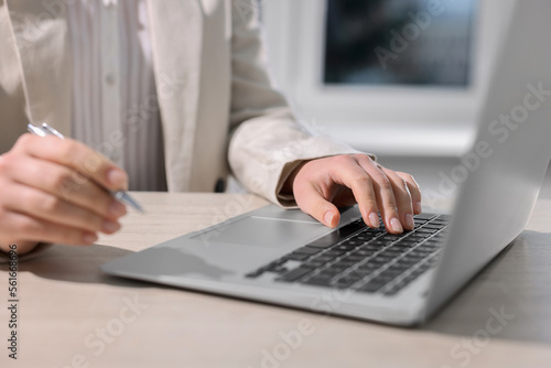 Woman with pen working on laptop at wooden table, closeup. Electronic document management