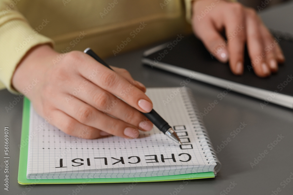 Fototapeta premium Woman filling Checklist with pen at grey table, closeup