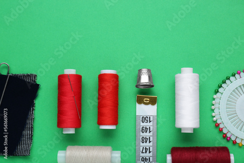 Flat lay composition with thimble and different sewing tools on green background. Space for text