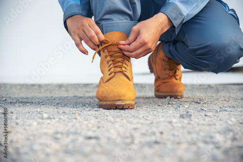 Man kneels down rope tie shoes industry boots for worker. Close up shot of man hands tied shoestring for his brown construction boots. Close-up man hands tie up shoes for footwear concept.
