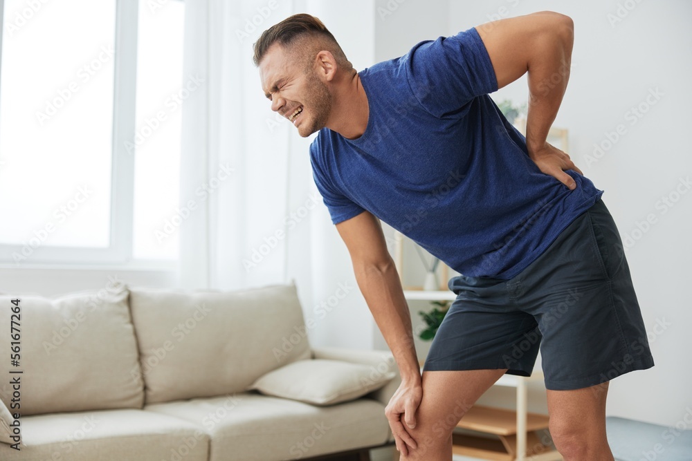 Man backache neck and shoulder pain, inflammation of muscles and ligaments rupture during sports, inflammation and injury, in a blue t-shirt at home Man backache neck and shoulder pain, inflammation of muscles and ligaments rupture during sports, inflammation and injury, in a blue t-shirt at home