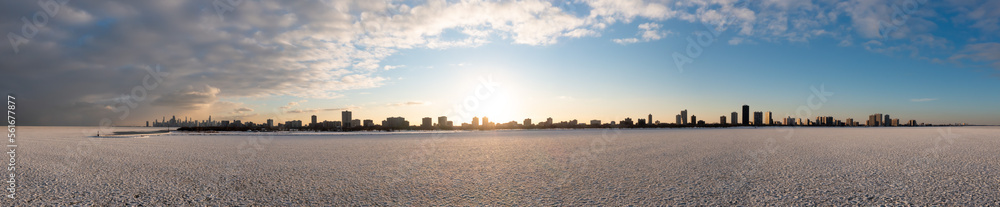 Fototapeta premium Wide angle aerial panorama of Chicago lakefront from the Edgewater neighborhood extending to Evanston on the right and downtown Chicago on the Left with clouds above and ice and snow below at sunset.