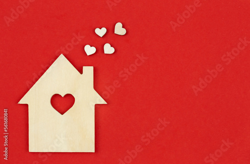 Wooden house with decorative hearts on a red background, flat lay, space for text.