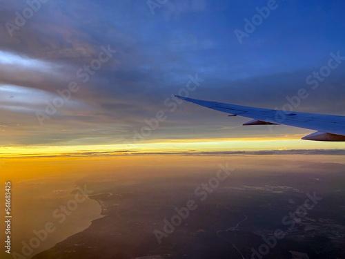 Though the window view over the wing of Aircraft air plane flying high altitude horizon and cloud daylight golden yellow sky 